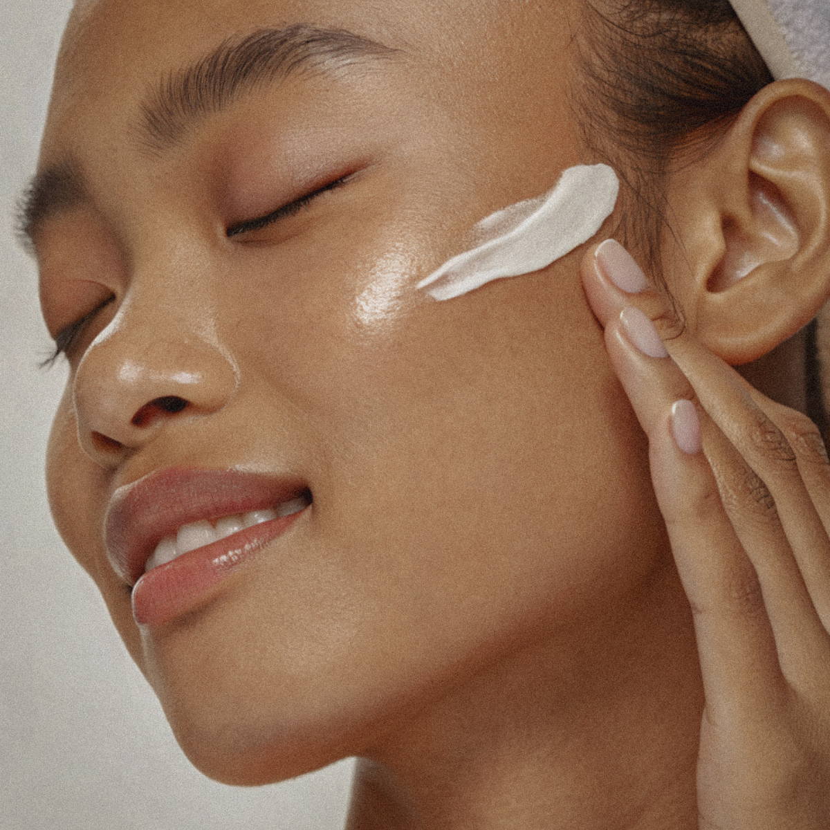 Close-up of a person applying cream to their face with a neutral background