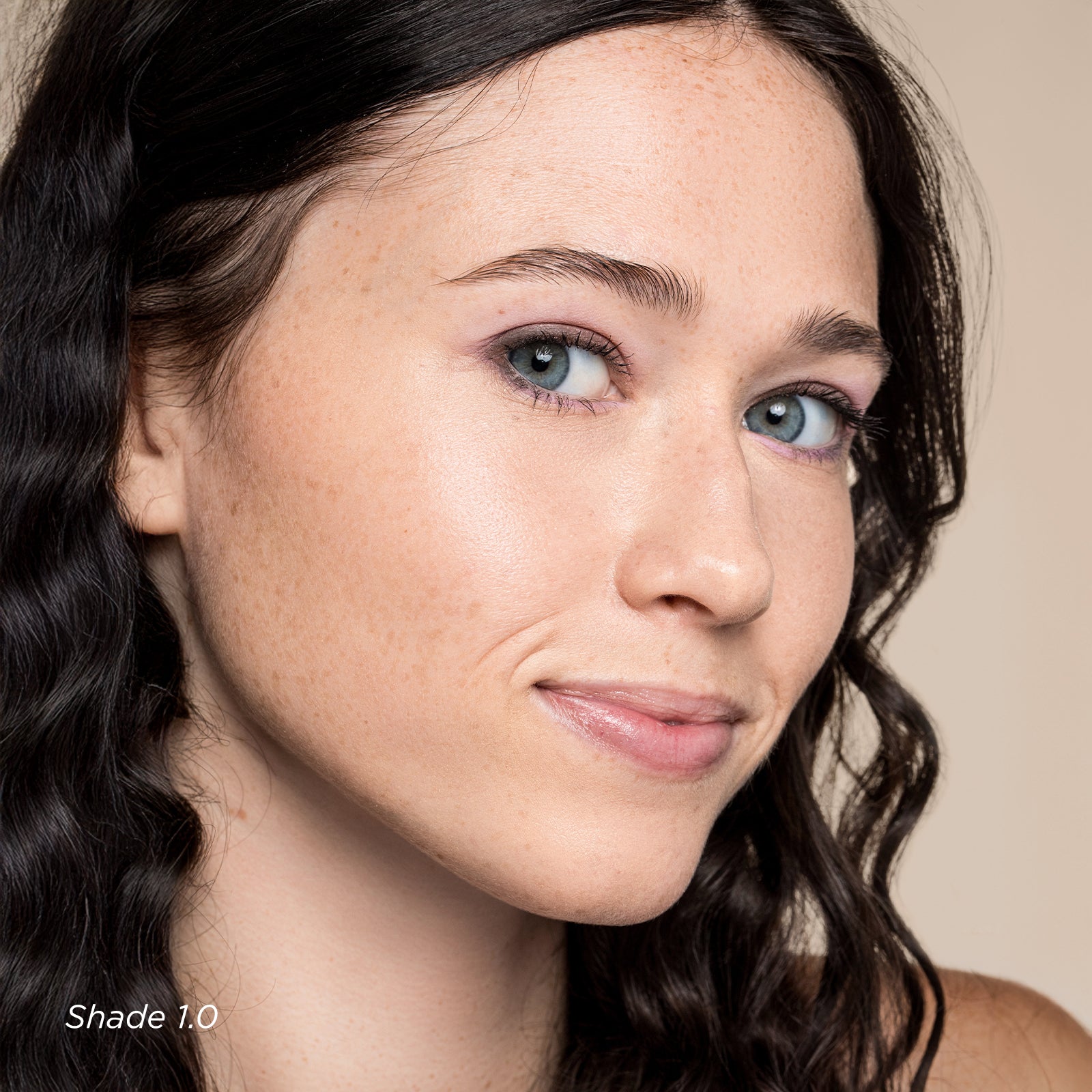 Close-up of a person with wavy hair and blue eyes on a neutral background
