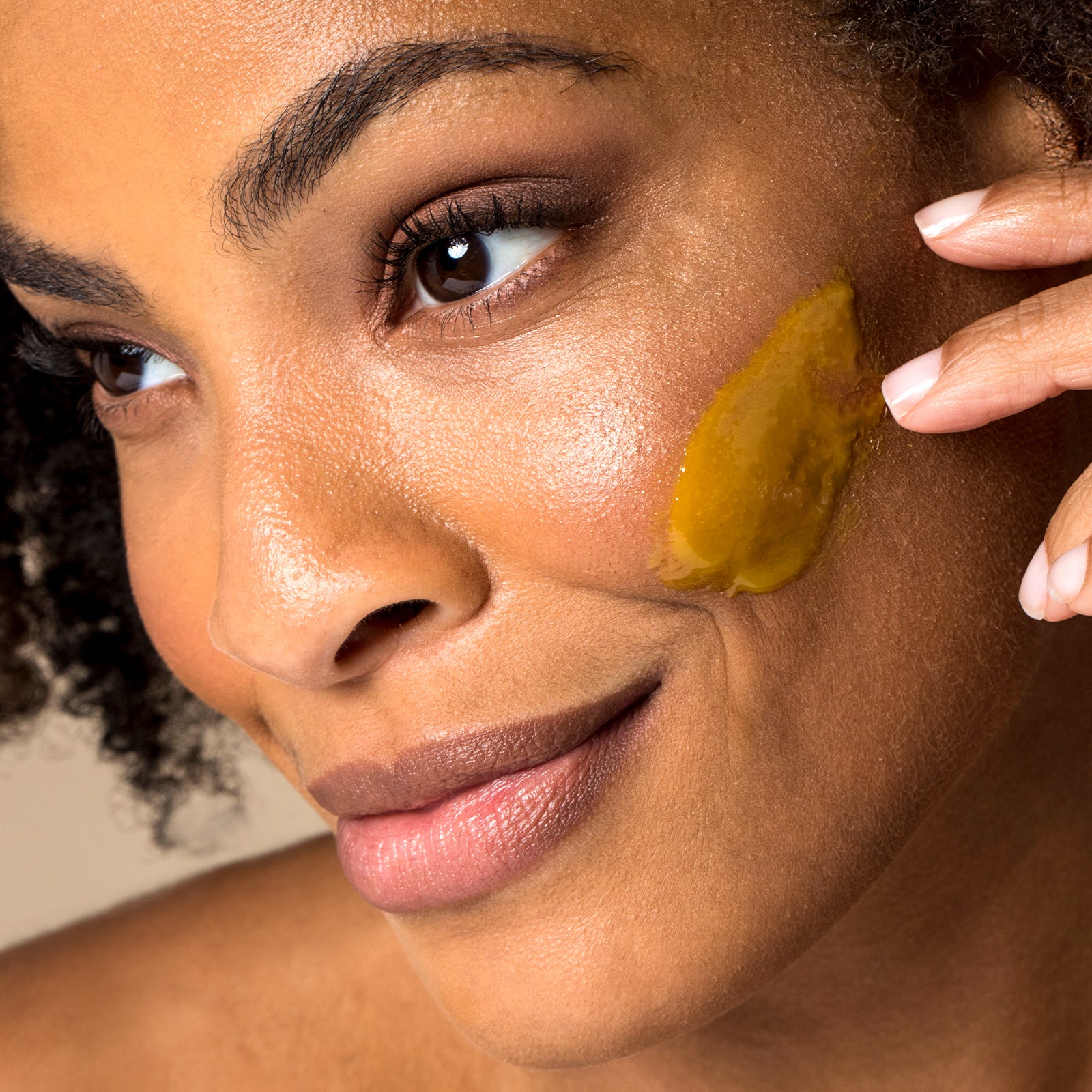 Woman applying a yellow facial mask to her cheek