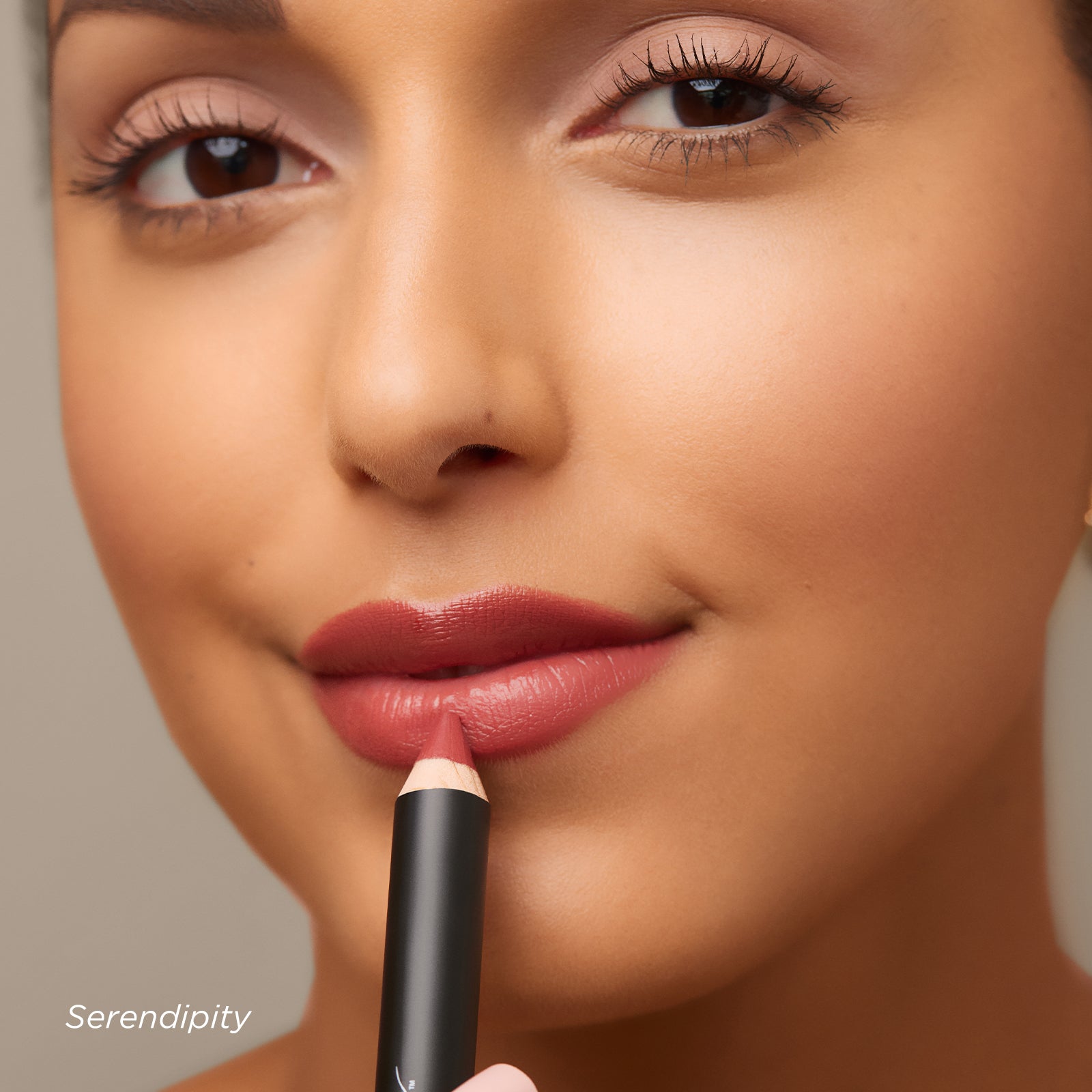Close-up of a woman applying lipstick with a pencil, on a neutral background.