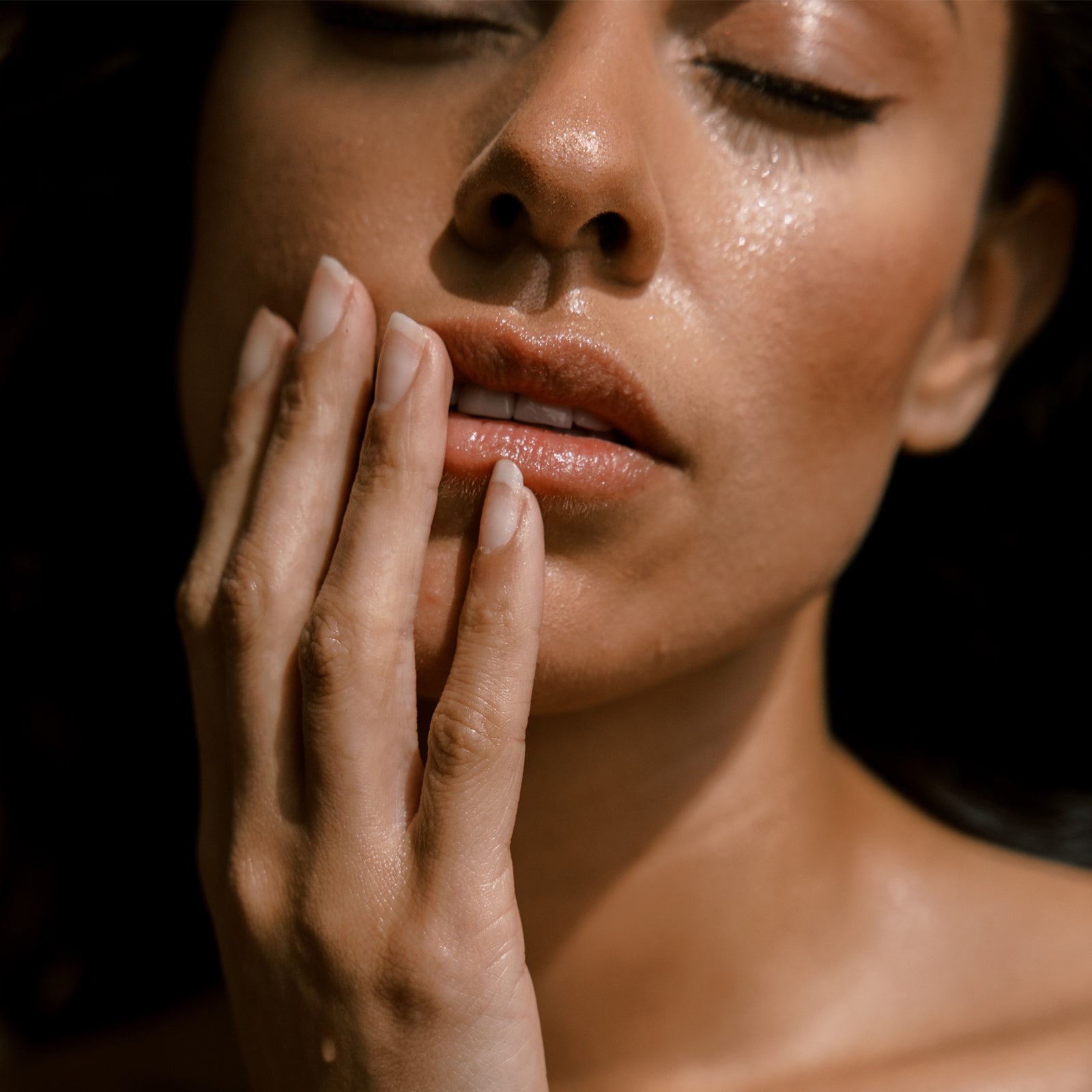 Close-up of a woman's face with her hand near her mouth against a dark background