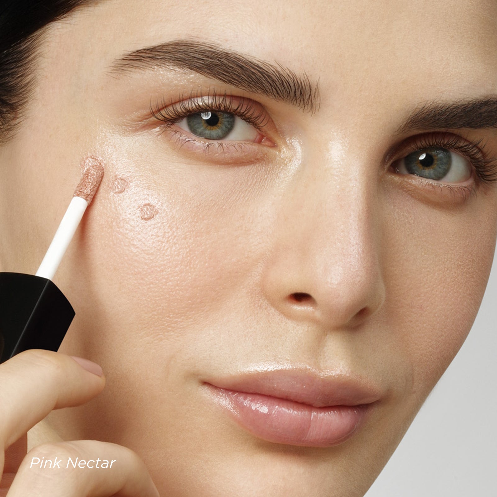 Woman applying a cosmetic product to her face with a brush labeled 'Pink Nectar'.