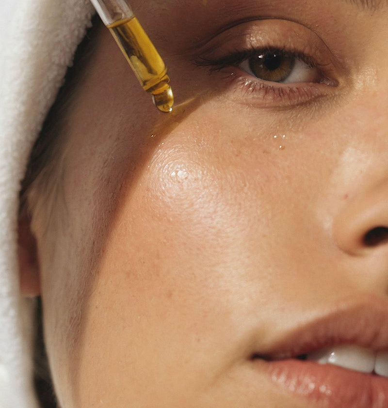 Close-up of a woman applying a dropper of oil to her forehead.